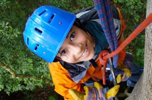 a smiling girl looks up as she begins to lower herself down from the canopy on a custom family trip in costa rica
