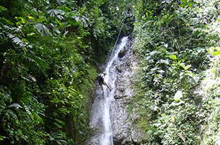 a wide view of a person lowering themselves down over a waterfall on a guided canyoning adventure in costa rica