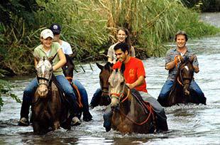 family laughing while horseback riding across deep river on private guided vacation in costa rica