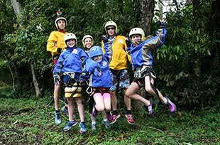 a family with small children jumps in the air to celebrate a successful canyoning adventure in costa rica