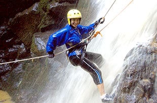 young woman in bright gear rappelling through a rushing Costa Rica waterfall
