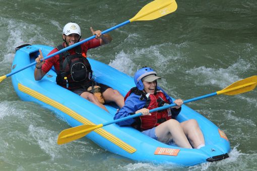 an excited woman and waving guide hold their oars up as they prepare for the whitewater in an inflatable kayak in costa rica
