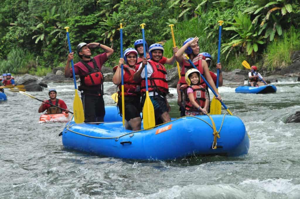 Serendipity Adventures Guide Mariano standing and saluting with a family in a whitewater raft on a river in Costa Rica