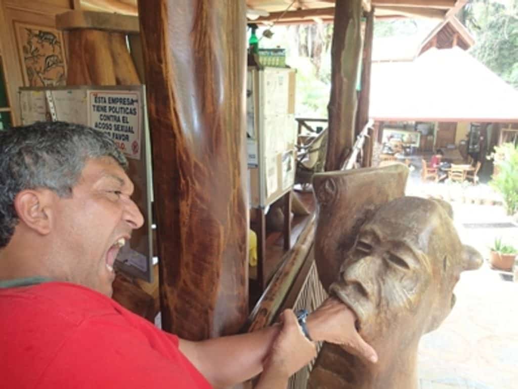 Serendipity Adventures Guide Mariano pretending to have his hand stuck in the mouth of a man's carved wooden head 