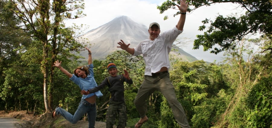 a family jumping with excitement with a view of the Arenal Volcano in the background