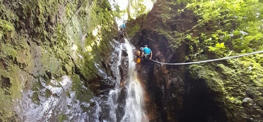a young woman using AFOs rappelling down a waterfall side by side with a canyoning guide on an accessible adventure in Costa Rica