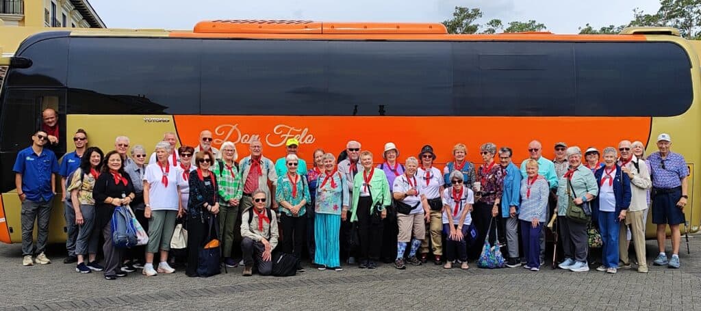 A group of senior travelers standing in front of an orange bus in Costa Rica